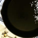 cast iron skillet with a little salt on a blue and white cloth and little brass spoon