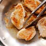 skillet of pan cooke chicken breasts with tongs