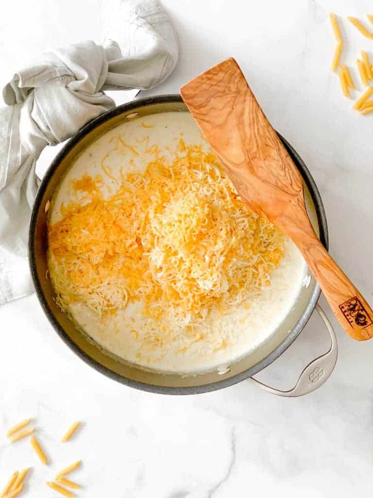 pot of white sauce with cheese and a wooden spatula.