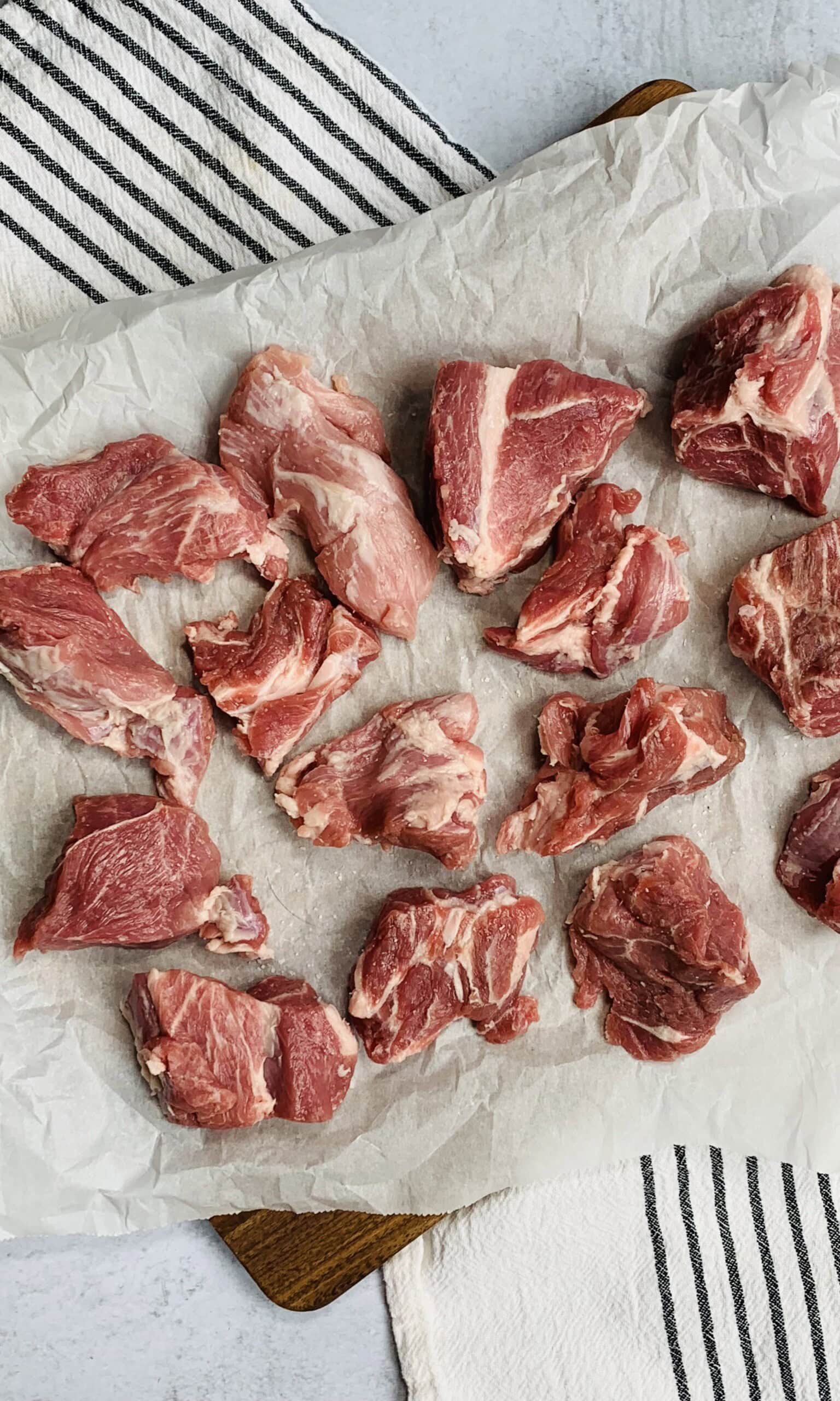 Raw pieces of boneless pork spread out on white parchment paper with a striped cloth partially visible underneath.