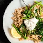 white dish with farro, English peas, asparagus and spinach with lemon and a white towel.