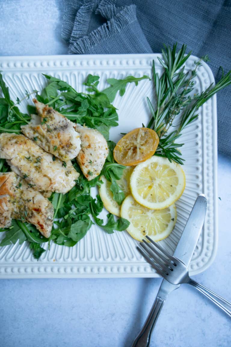 sous vide chicken with lemon and roasted garlic and rosemary on a white platter with utensils and a gray napkin.