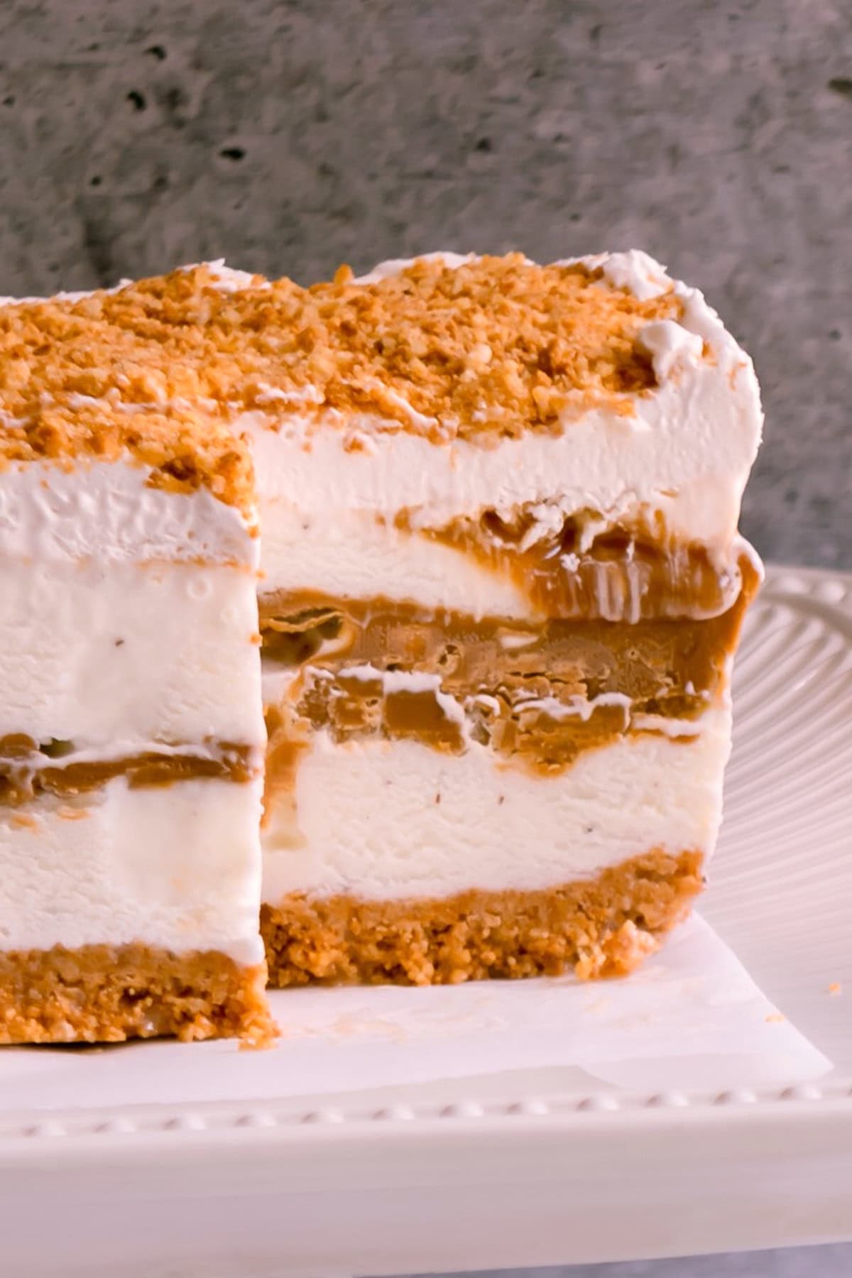 A layered ice cream cake with a amaretti crust, vanilla ice cream and cookie butter filling, and a crumbled topping on a white plate.
