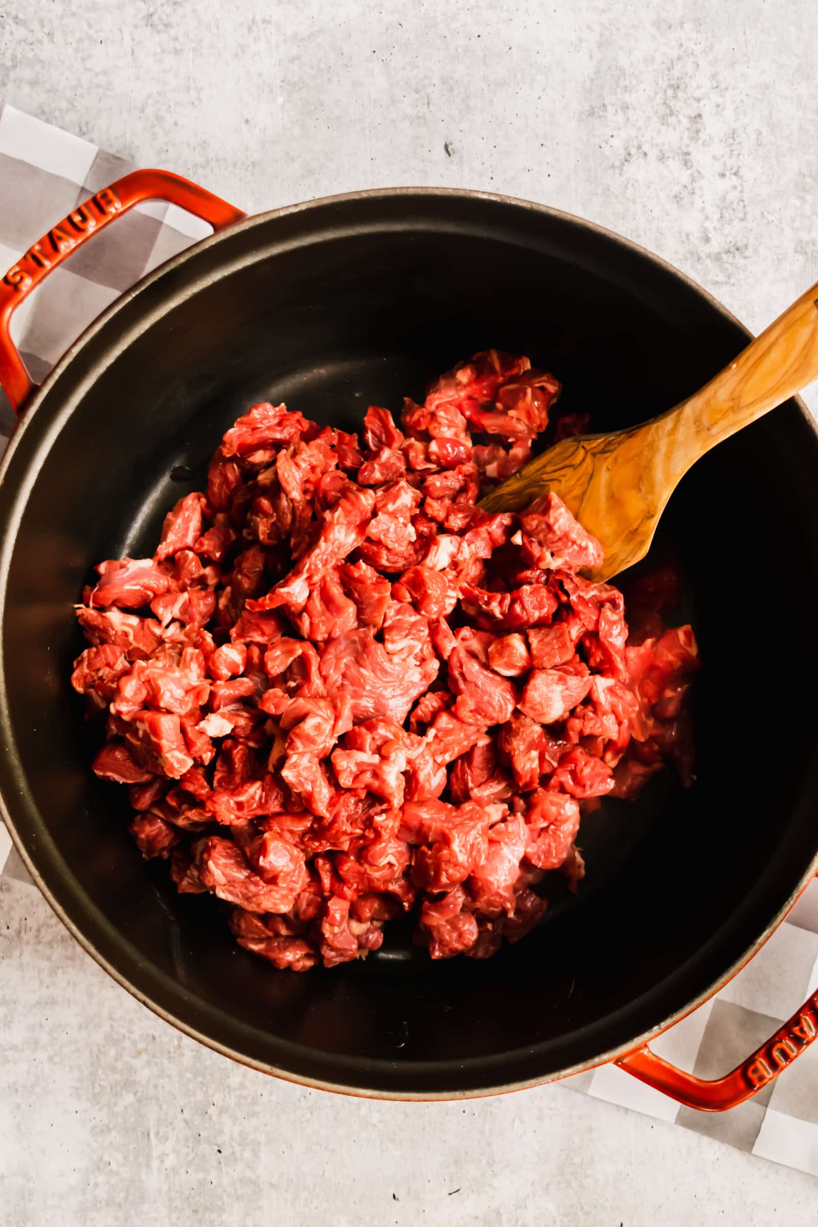 black dutch oven with chopped steak being cooked and sauteed with a wooden paddle.