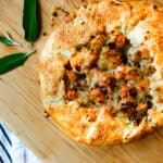 Closeup of butternut squash and gruyere crostata on a wooden pizza peel with sage leaves on a white dish towel with black stripes.
