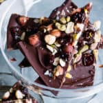 close up of pieces of dark chocolate espresso bark with cherries, pistachio and hazelnuts on a glass pedestal.