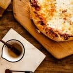 cast iron skillet pizza on a wooden peel with honey glaze next to it in a white bowl.