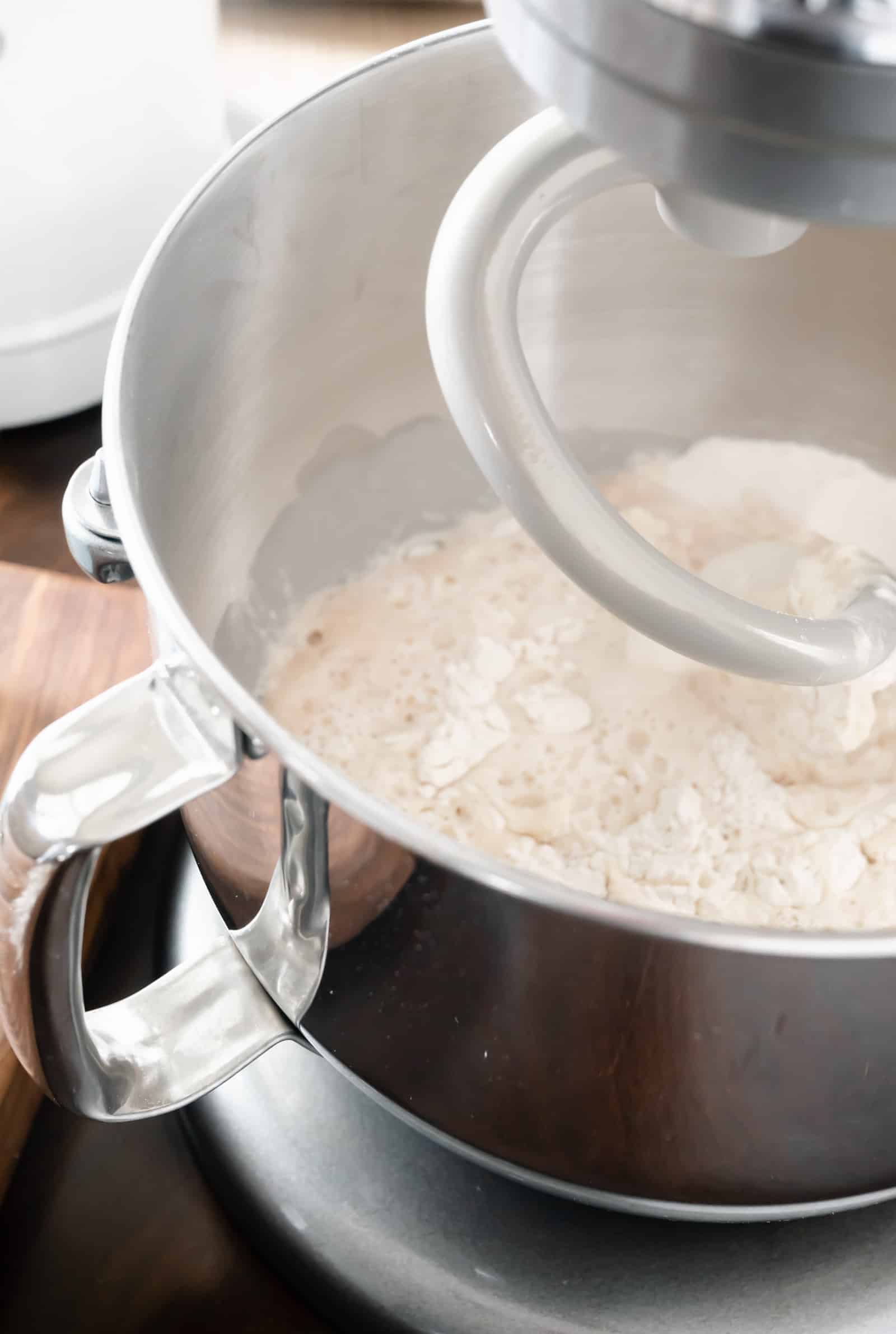stand mixer with dough hook with bowl of pizza dough ingredients.