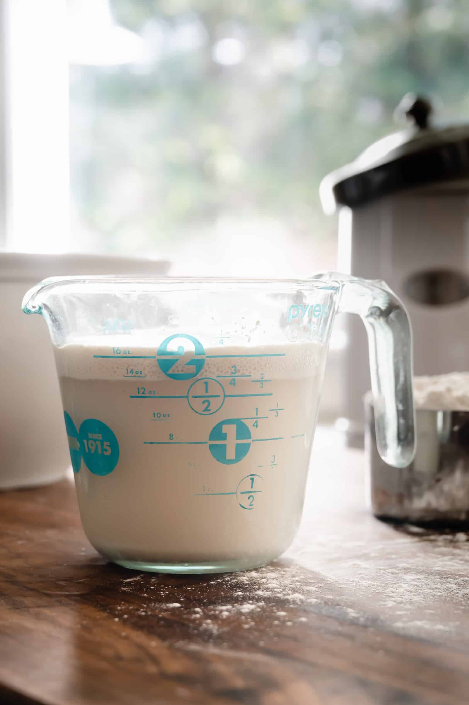 glass measuring cup of foamy yeast and water next to mixer.