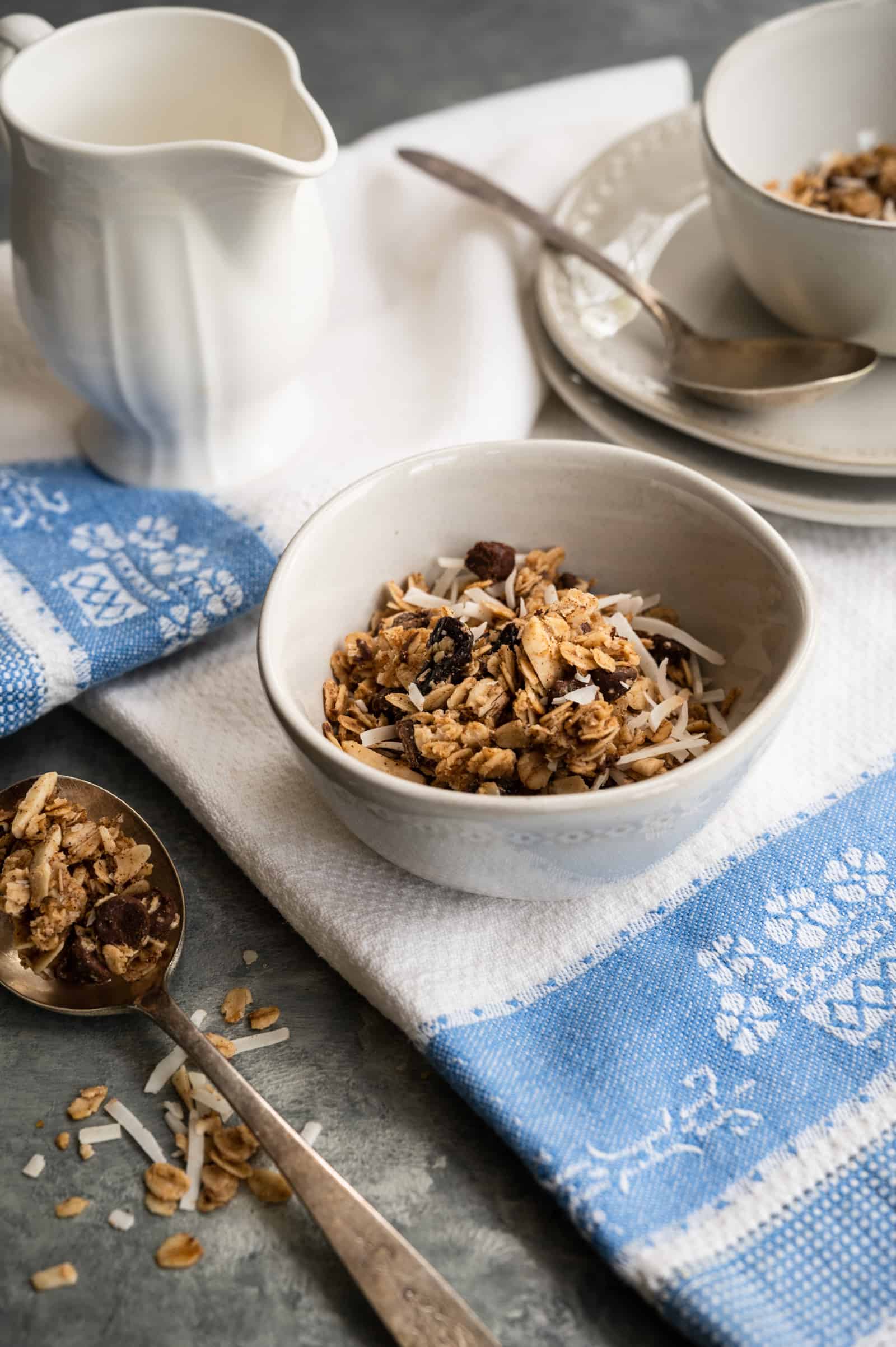 white bowl with vanilla granola on a blue and white towel with bowl and plates in background.