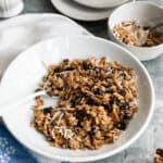 white bowl with vanilla granola on a blue and white towel with bowl and plates in background.