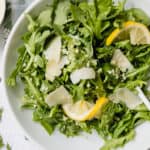 white bowl of arugula, parmesan and lemon slices on a green and white floral napkin.