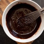 white bowl with chocolate ganache and a whisk on a wooden cutting board.