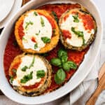 white pan of baked breaded eggplant with tomato sauce, cheese and basil.