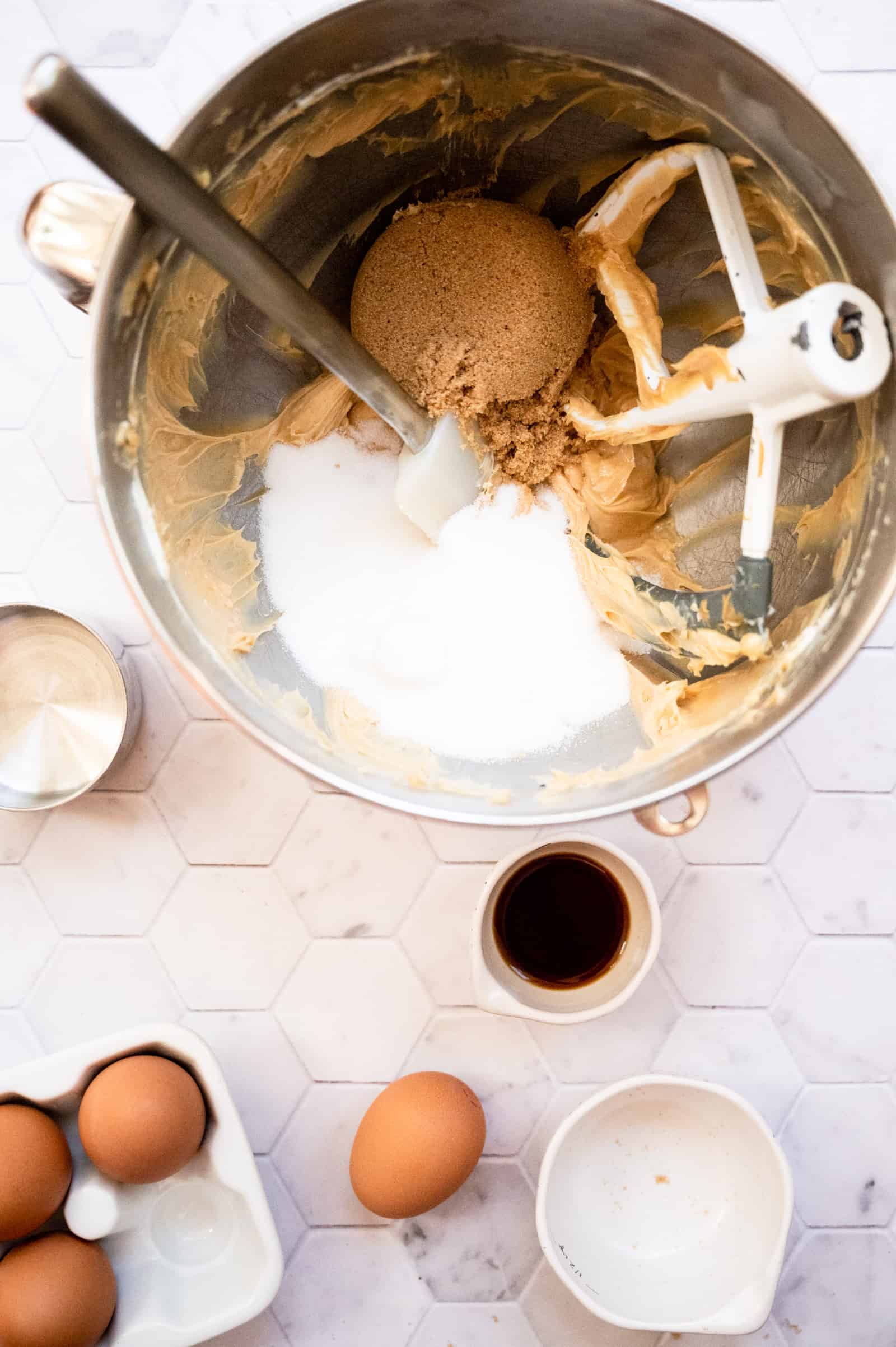 mixing bowl with cookie dough, brown sugar, sugar and some vanilla and more eggs on a marble background.