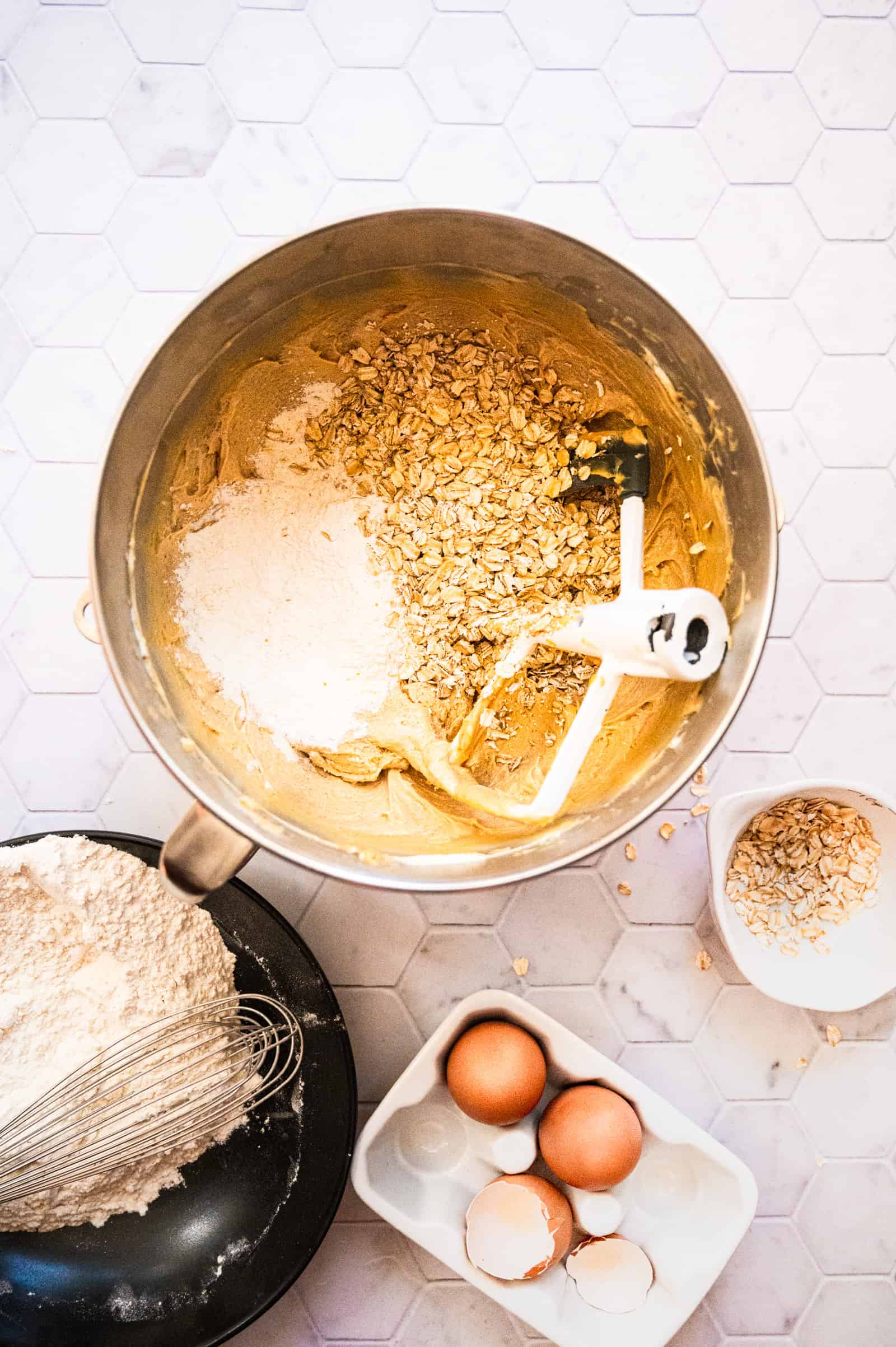 mixing bowl and assorted bowls with cookie dough, oatmeal, flour and eggs on a marble background.