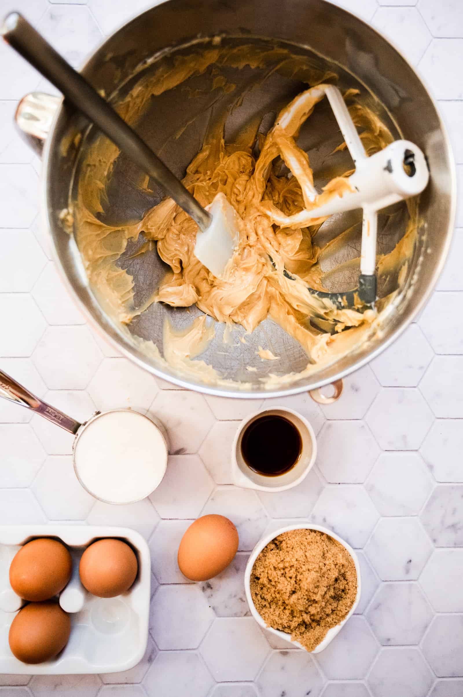 overhead shot of creamed butter and sugar in a mixing bowl and small bowls and cups of sugar, vanilla, and small carton of eggs.
