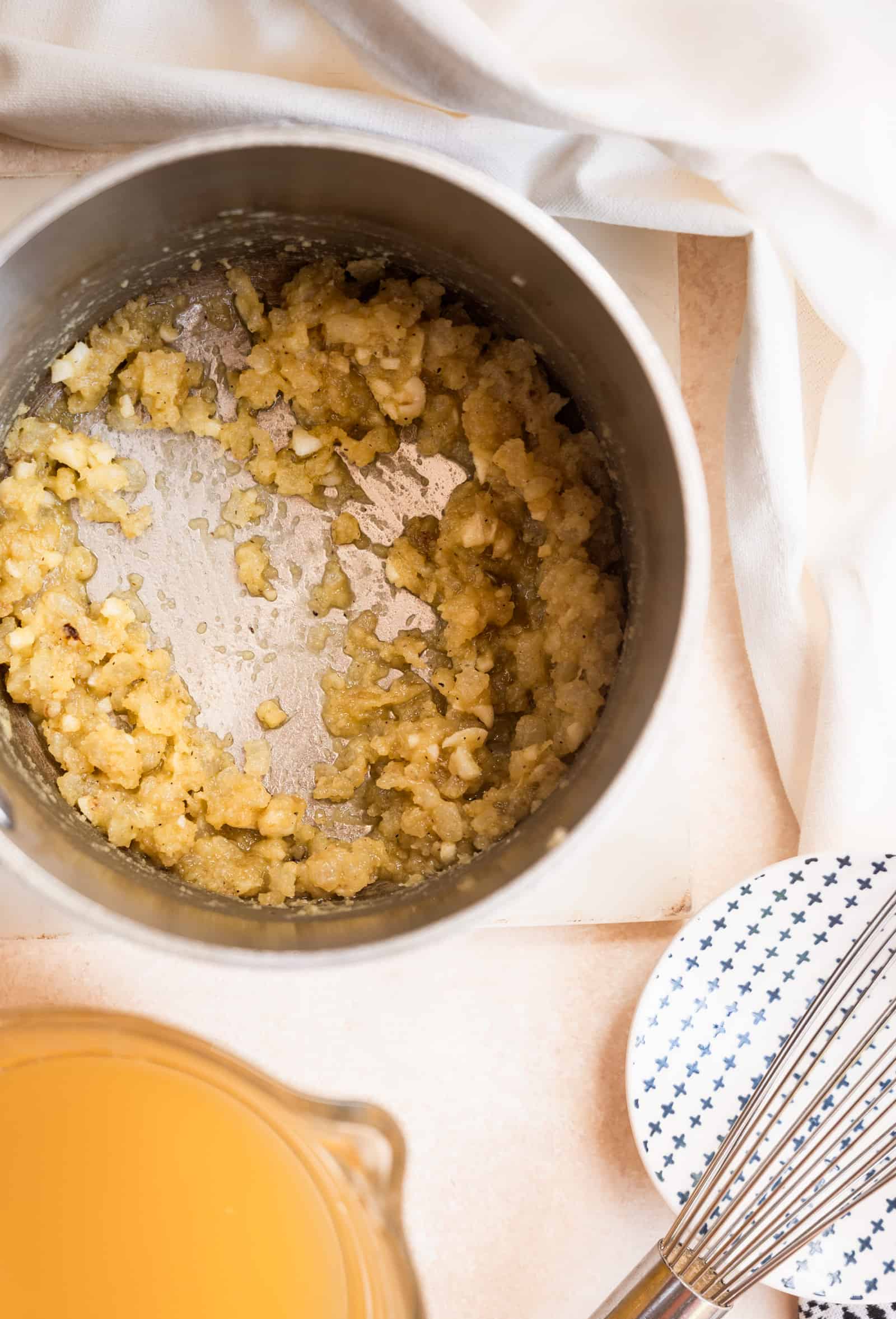 roux with onions and a glass measuring cup of chicken broth.