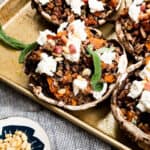 baking tray with stuffed portobello mushrooms with a bowl of pine nuts.