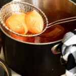 a strainer with cooked onions sitting over a saucepan of tomato sauce.