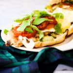 a white plate with a grilled chicken sandwich on a blue and green plaid napkin.