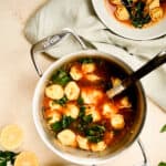 stockpot of tortellini soup with two white serving bowls of soup with spoons in them.
