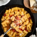 cast iron skillet with rigatoni, tomatoes, parmesan cheese on a dark background.