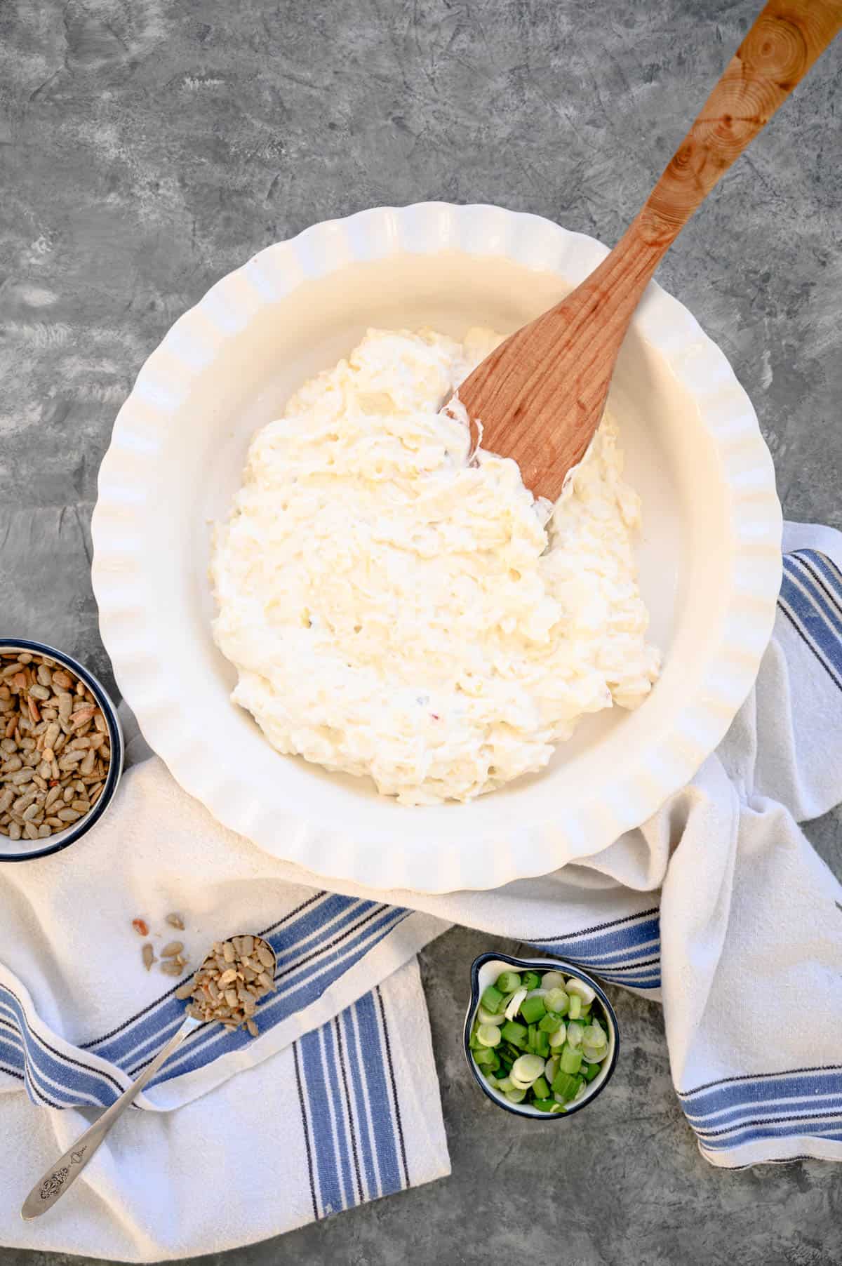 wooden spoon spreading white cheese dip into a white fluted pie plate.