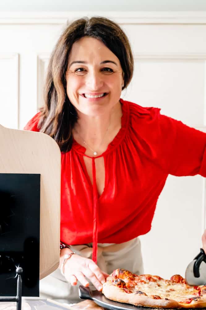 women in red shirt smiling and cutting pizza.