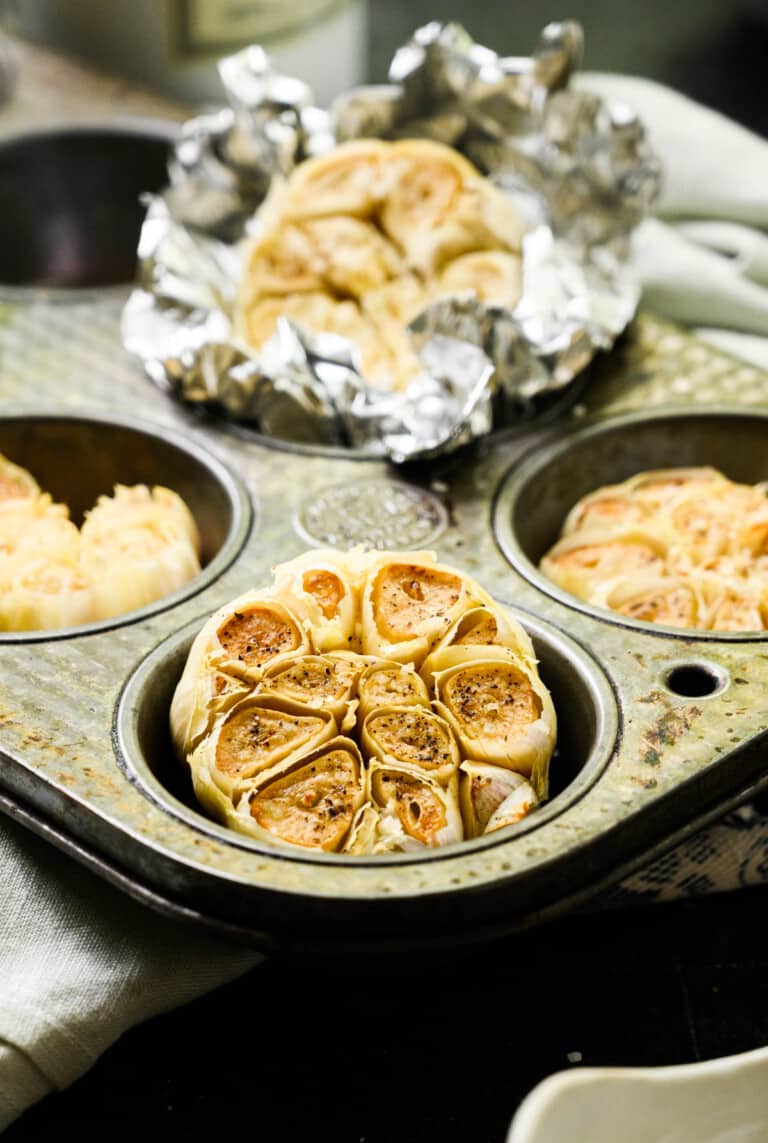whole heads of roasted garlic in a muffin tin.