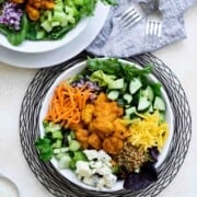 Two white bowls of salad ingredients including some buffalo chicken and crumbled blue cheese