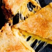 three triangles of grilled cheese melted all over the sandwich on a dark black background.