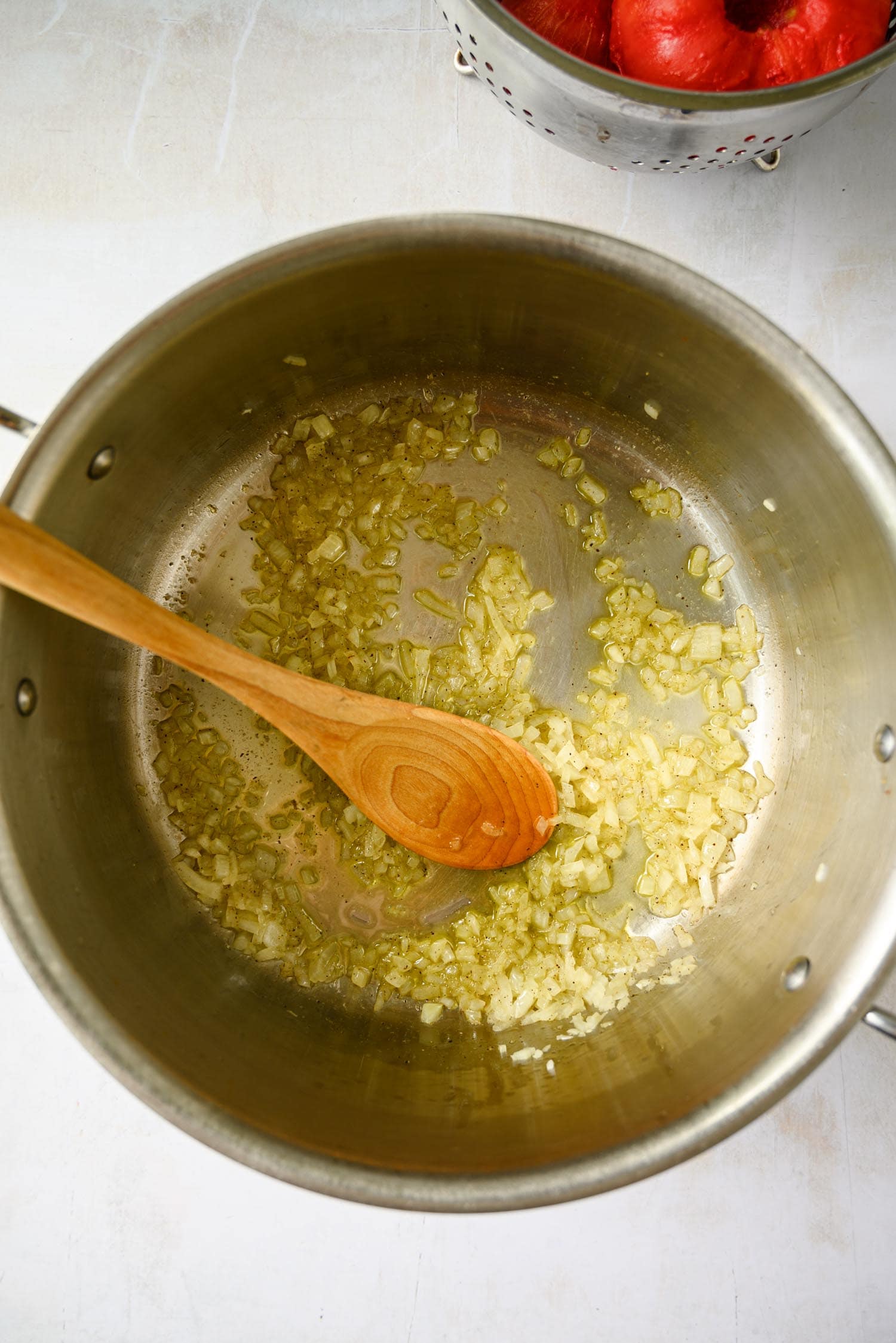 A large metal pot with sautéing onions, stirred by a wooden spoon, for tomato marinara sauce.