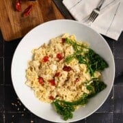 large white serving bowl of creamy bowtie pasta topped with broccolini and red chiles.