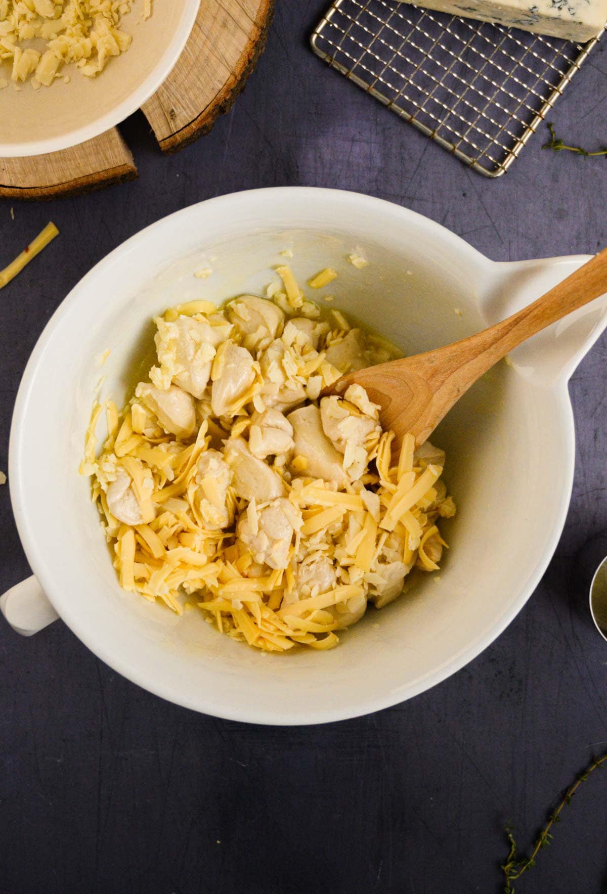 A wooden spoon mixing bite-sized biscuit pieces and shredded cheese for cheesy monkey bread in a white bowl.