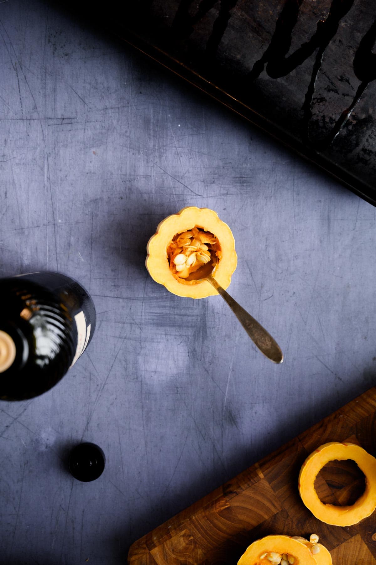 A halved delicata squash with seeds and a spoon inside sits on a gray surface.
