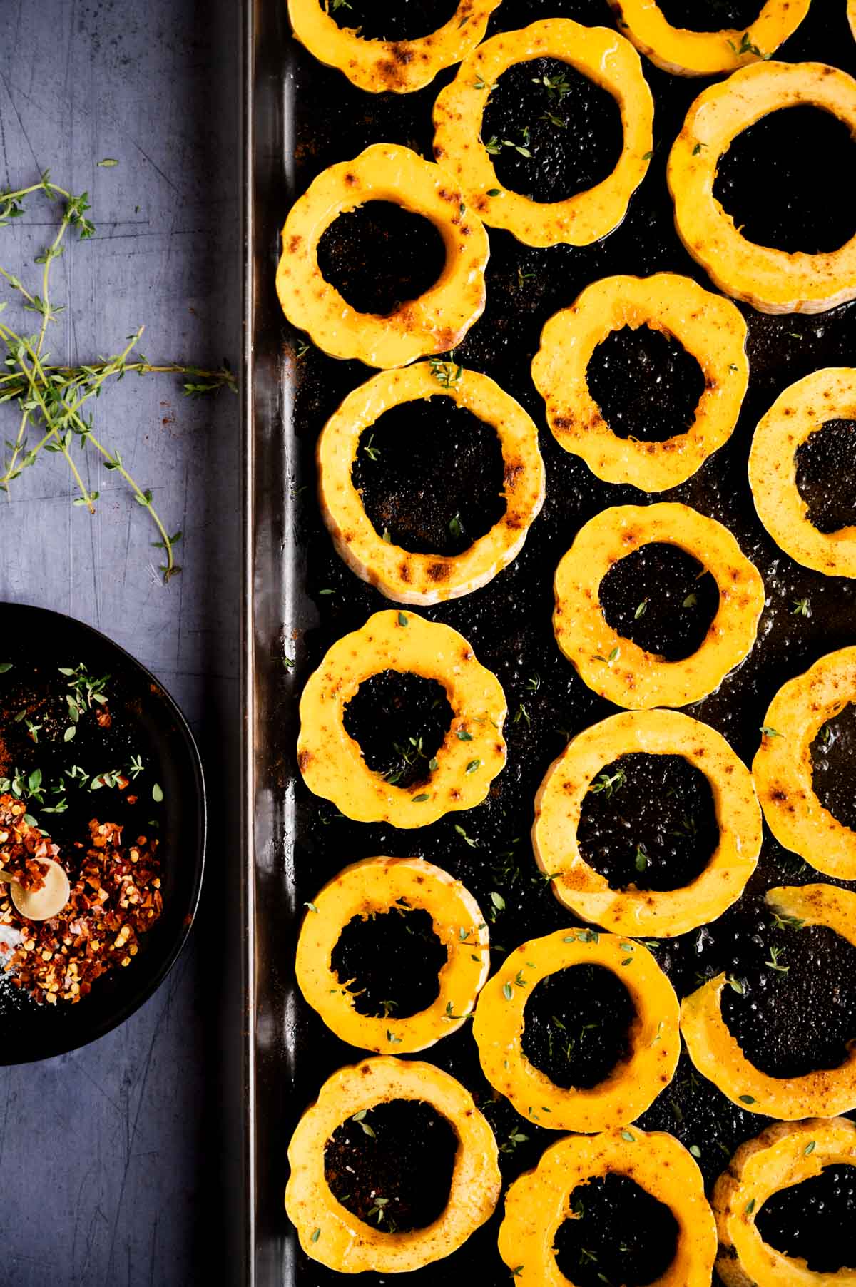 Rings of prepped delicata squash are arranged on a dark baking sheet.