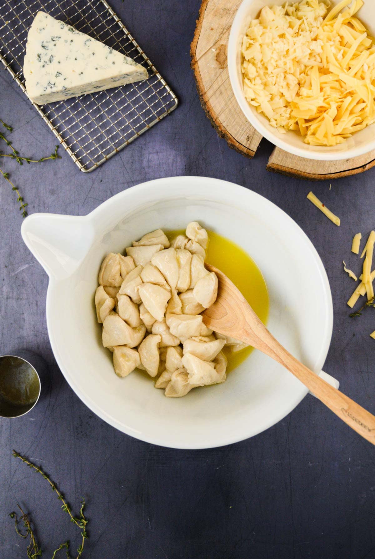 Dough pieces for cheesy monkey bread in a mixing bowl with melted butter and a wooden spoon, flanked by a wedge of blue cheese and a bowl of shredded cheese.