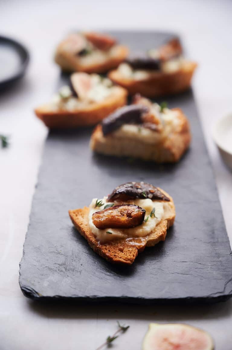 zoom of black slate with piece of toasted bread spread with ricotta cheese topped with figs and thyme.