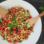 large white bowl of chickpea salad with fresh mint and dill leaves.