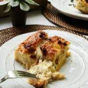 Fork pulling a cheesy bite of egg casserole on a white plate near a potted succulent plant.