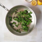 Skillet of cooked broccolini with lemons and salt.