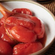 white bowl with canned tomatoes and a wooden spoon on woven mat.