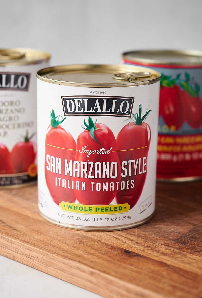 three cans of San Marzano tomatoes on a wooden board.