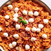 skillet with bowtie pasta and vodka sauce with fresh mozzarella balls and basil leaves.