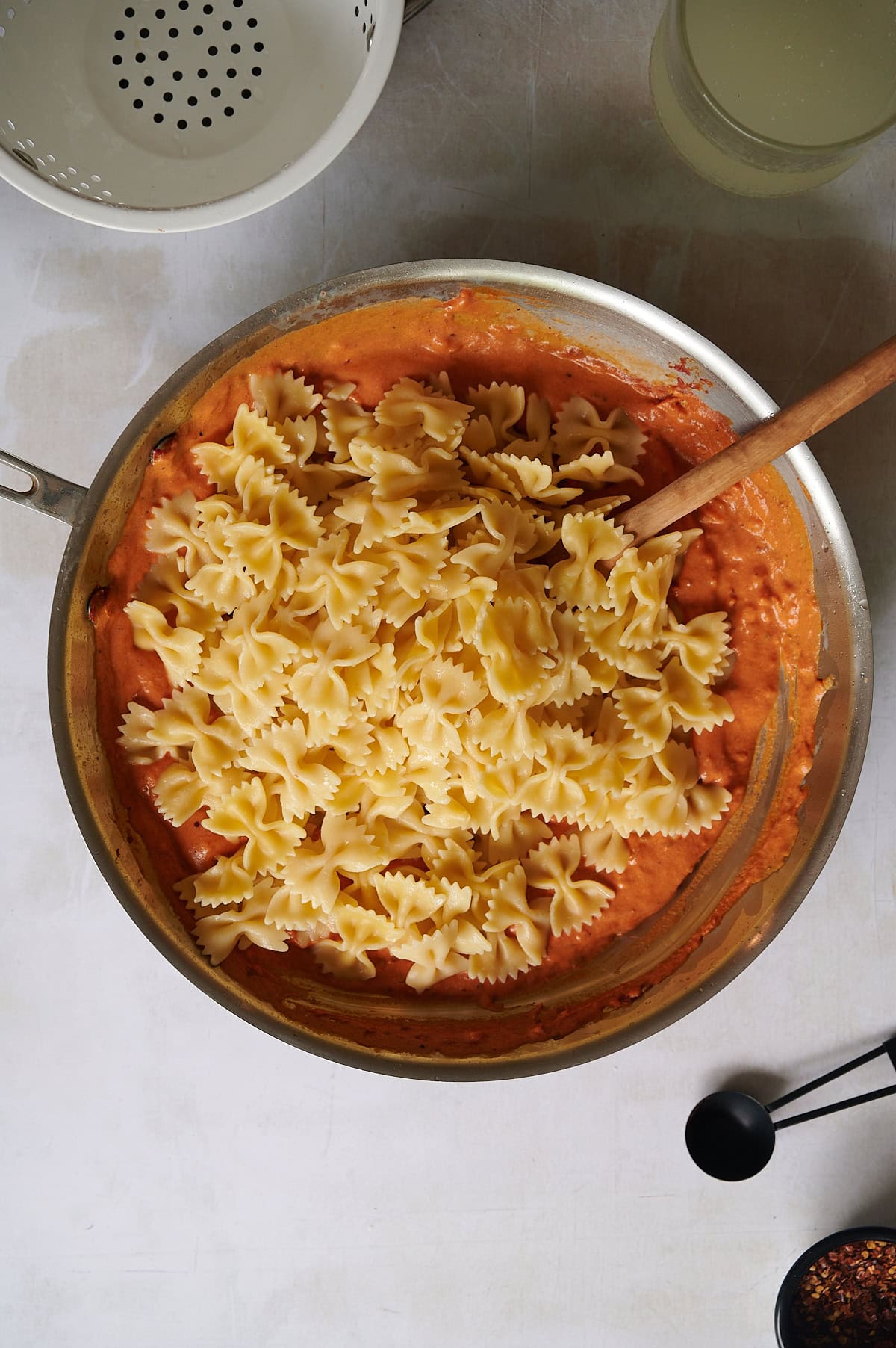 Farfalle pasta is added to vodka sauce with a wooden spoon resting inside, ready to be mixed.