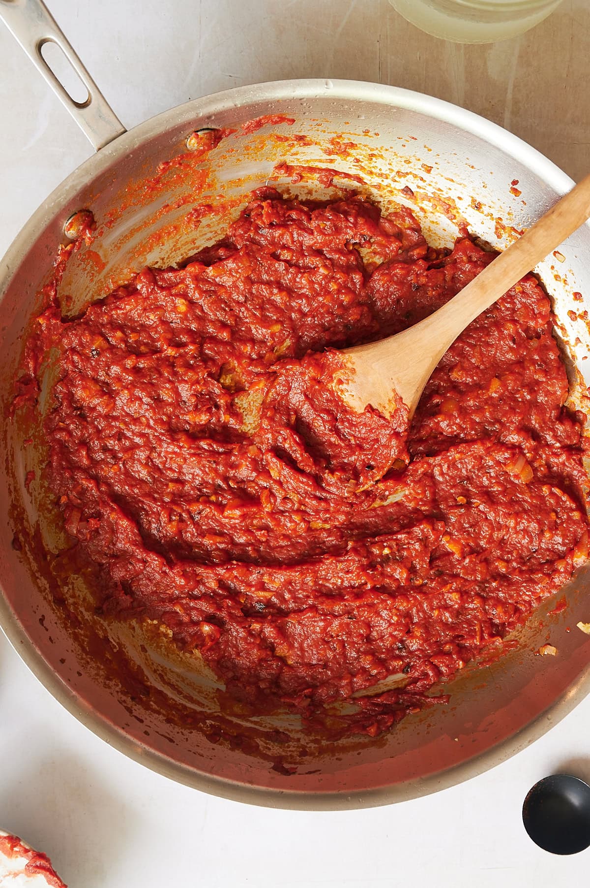 A stainless steel skillet filled with thick, spicy vodka sauce with pancetta is being stirred with a wooden spoon, viewed from above.