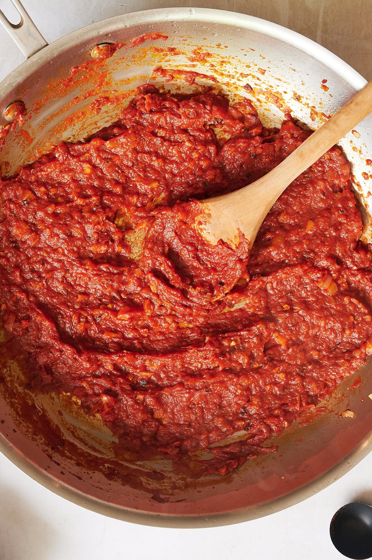 Vodka is being simmered to cook off tomato paste for vodka sauce and being stirred with a wooden spoon in a metal pan.