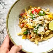 hand reaching for a bowl of pepper, chicken and gemelli pasta.