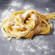 floured and cut homemade pasta that is nested on a gray background.